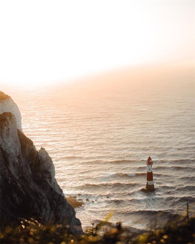 denizde bir deniz feneri etrafa saçılmış bir kaya ve güneş yatay olarak solgun duvar kağıdı