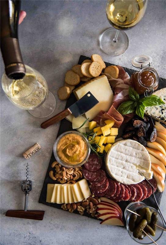 krožnik na mesni plošči s siri in dvema kozarcema vina na marmorni mizi