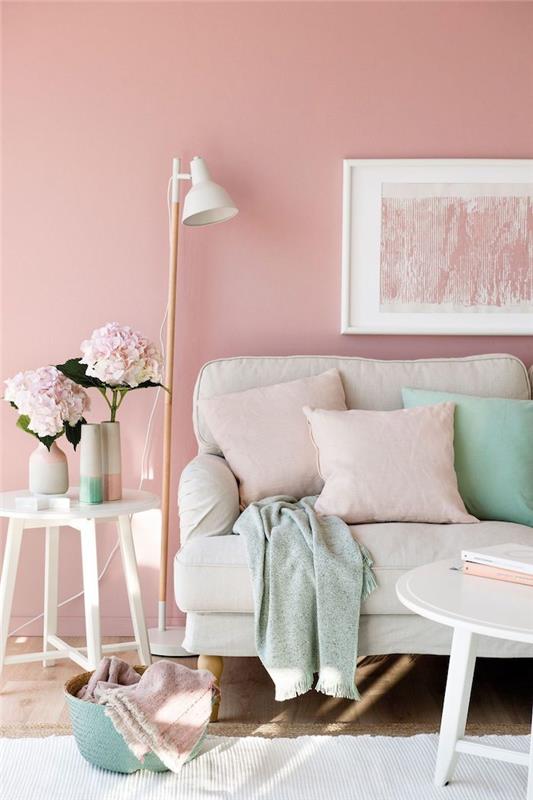 dnevna soba z rožnatimi stenami za bež kavčem, okrašeno z metinimi zelenimi blazinami in praškasto rožnato sliko, ki visi