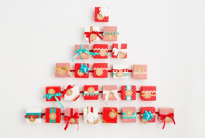 mažos dovanėlės raudonose ir baltose miniatiūrinėse dovanų dėžutėse ant raudonos juostelės juostelės Kalėdų eglutės formos ant baltos sienos, personalizuotas advento kalendorius