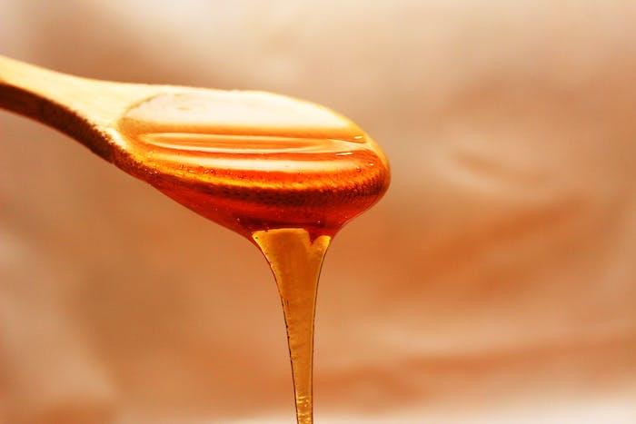 lesena žlica, polna medu z oranžnim ozadjem