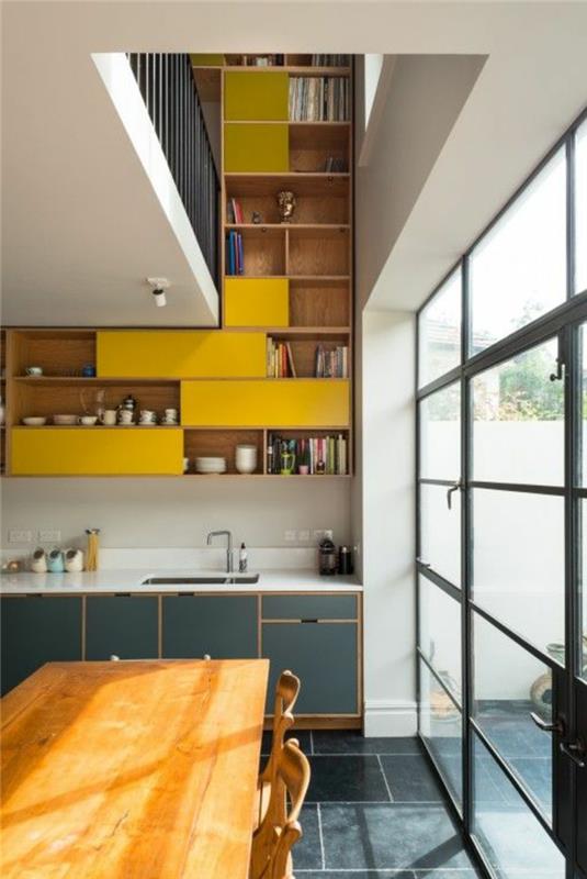 perlų pilka ir geltona virtuvės pertvarka, perdažyta virtuvė, baltos lubos, lentynos iš dalies šviesios medienos ir iš dalies geltonos, stumdomos stiklinės durys į terasą