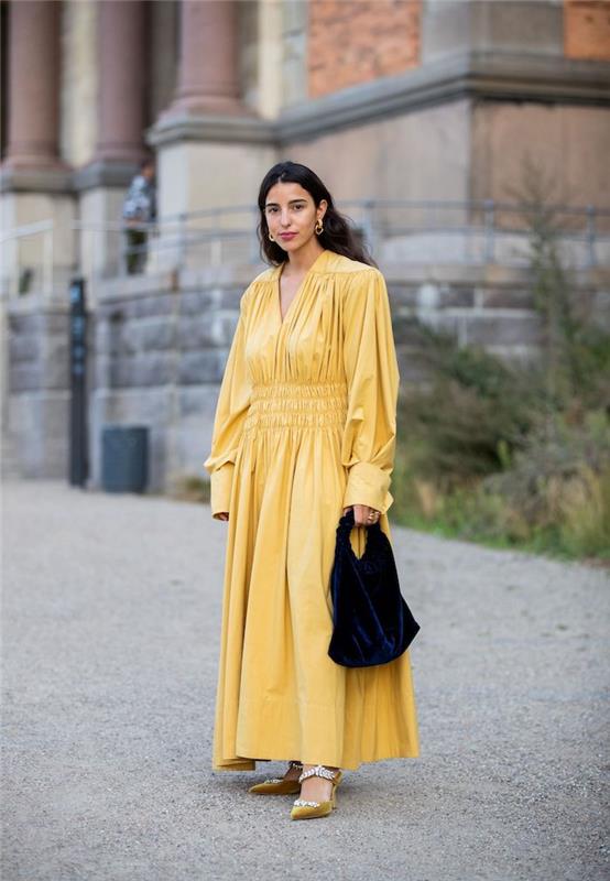 el çantası olan uzun sarı bir elbise giymiş bir kadın kültürel bir binanın önünde boğuldu