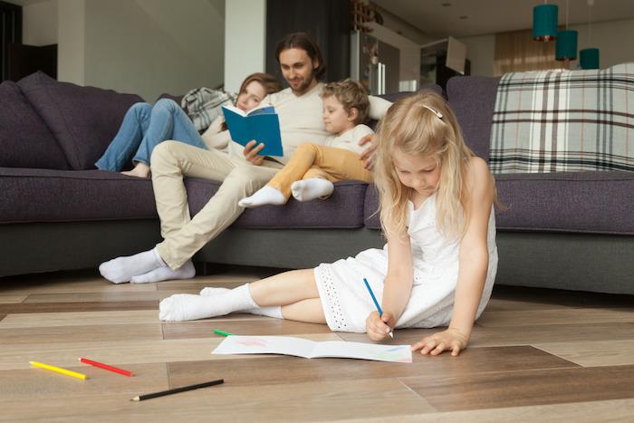 dukra žaidžia ant grindų, o tėvai ir sūnus skaito knygą