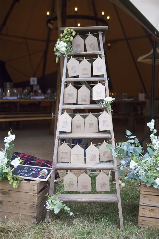 „pasidaryk pats“ vestuvių stalo plano idėja, pagaminta iš vintažinių medinių kopėčių su kraftpopieriaus svečių sąrašo etiketėmis, gėlių dekoru, linine virve ir pakabinamais skalbinių segtukais