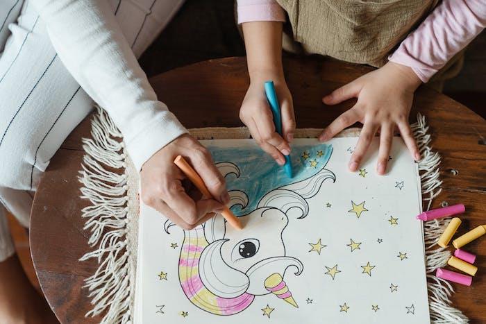 maža mergaitė ir jos mama piešia vienaragį ant balto popieriaus