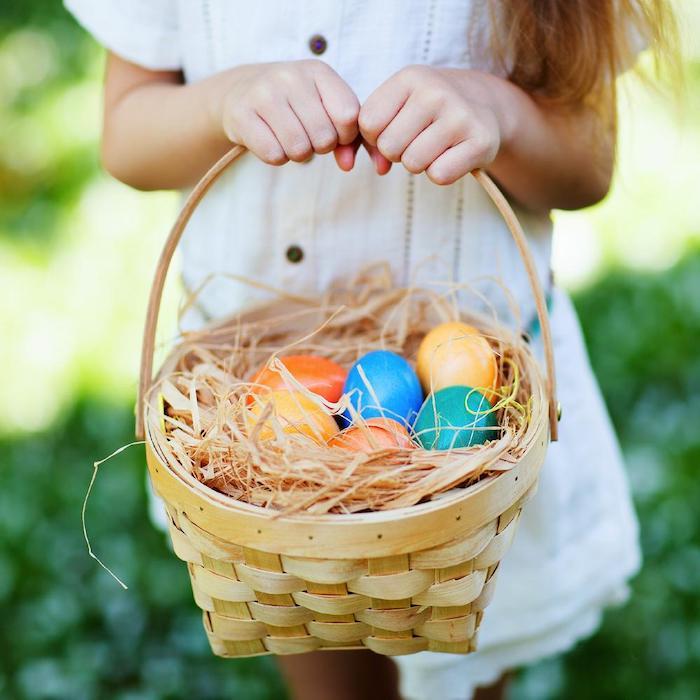 küçük bir kız elinde sahte ot ve boyalı yumurtalarla dolu dokuma bir sepet tutuyor.