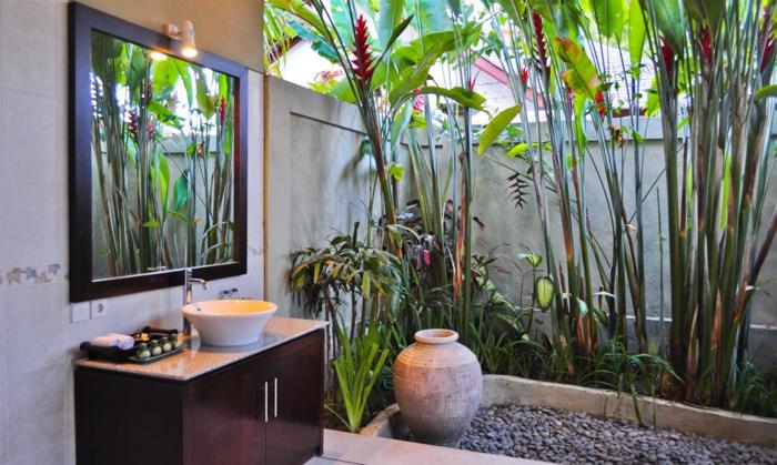 žalias vonios kambarys, didelis veidrodis su juodu rėmu, spinta tamsiai rudos spalvos, aukštų egzotinių augalų, kambarinių žalių augalų