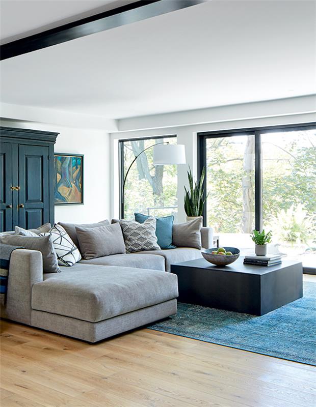 dnevna soba z velikimi okni, turkizna preproga in siv kotni kavč v barvi deco trend 2021