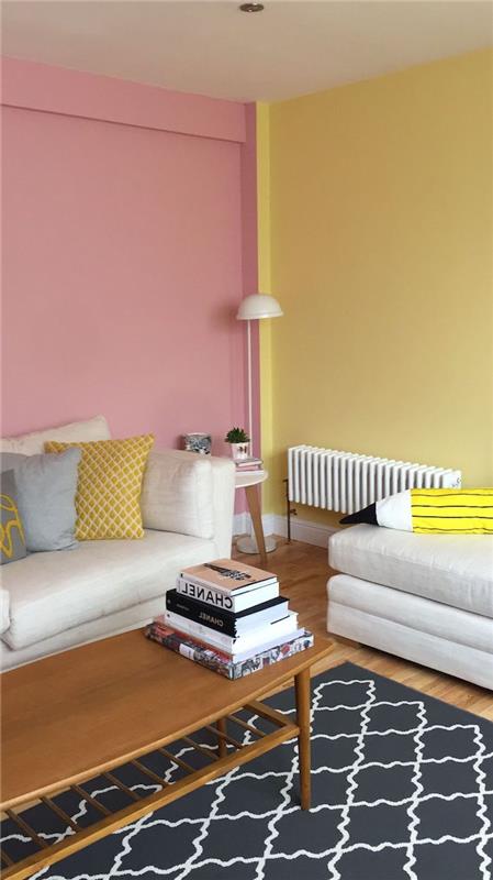 dnevna soba s praškasto rožnato steno in rumeno stensko leseno mizo na sredini nad okrašeno preprogo