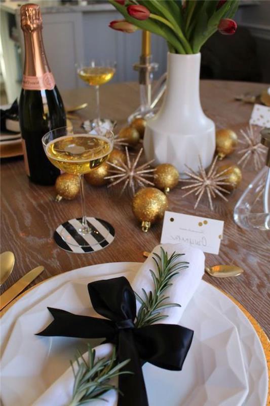 okrašena novoletna miza z zlatimi kroglicami rožmarinovih vej in zraven tulipani steklenico šampanjca