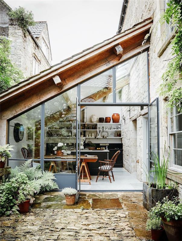 veranda ob hiši, zaščitena s stekleno streho in obdana z zelenimi rastlinami
