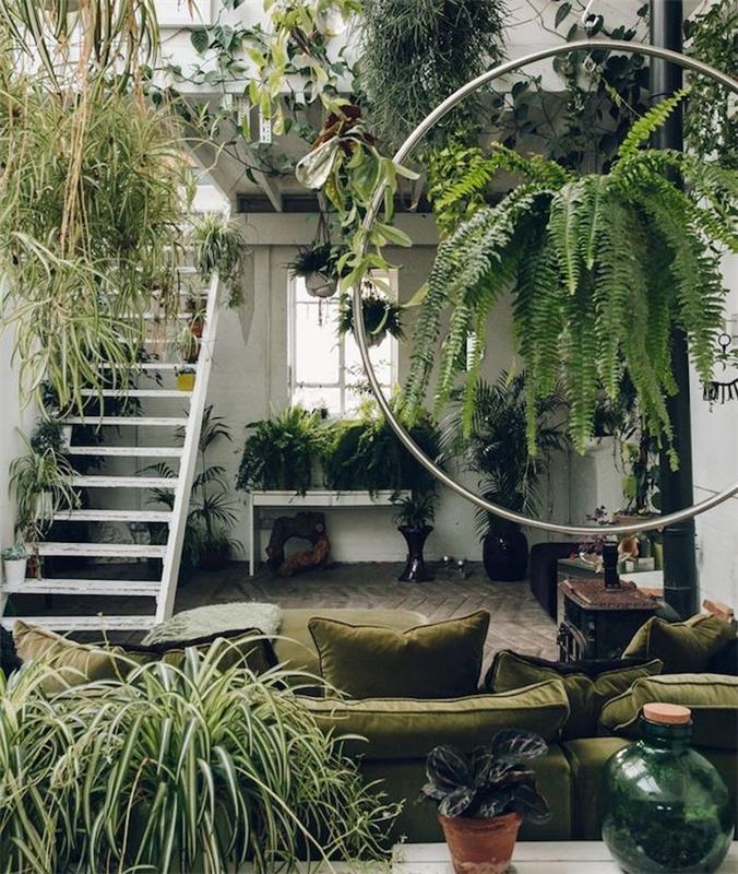 dekoracija v džungli v poraščeni dnevni sobi, oljčno zelen kavč, belo stopnišče, več visečih rastlin