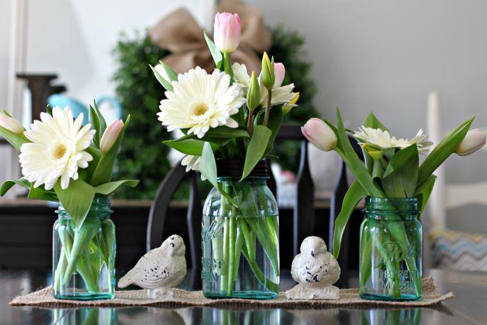vaza za kozarec in cvetlični lonec na tekaču za mizo iz jute in izvirne figurice ptic, okras pomladne mize