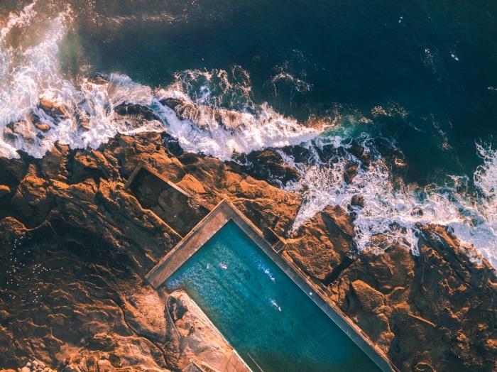 nemokama ekrano užsklanda su jūros vaizdu, ant uolos lūžtančių bangų ir didelio atviro baseino nuotrauka