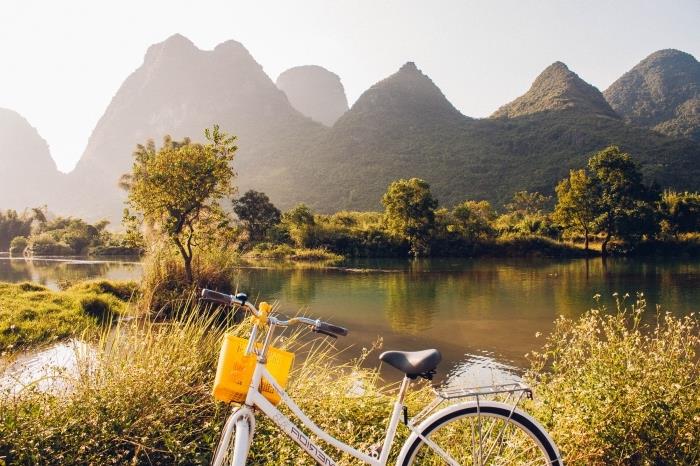 gražių tapetų pavyzdys su baltu ir juodu dviračiu priešais didelį ežerą ir žalias kalnų kalvas, apšviestas saulės spindulių