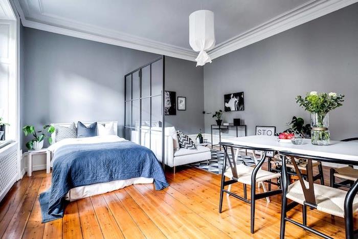 majhno stanovanje z jedilnico, spalnica z modro -belim posteljnino, steklena pregrada ob sivo -beli dnevni sobi