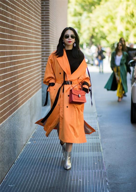 turuncu trençkot, gümüş renkli çizmeler, zincir omuz askılı kırmızı çanta, siyah kazak