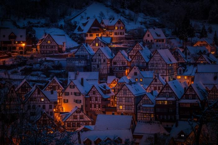 kaimas Vokietijos Alpėse, prieblanda, vasarnamio stiliaus namai, apšviesti švelniomis šviesomis, sniego viršūnė