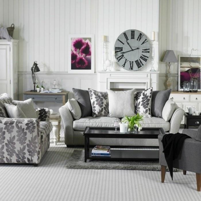 pilka sofa -lova, metalinis juodas kavos staliukas, senovinis laikrodis, virš židinio, pilkas kilimas
