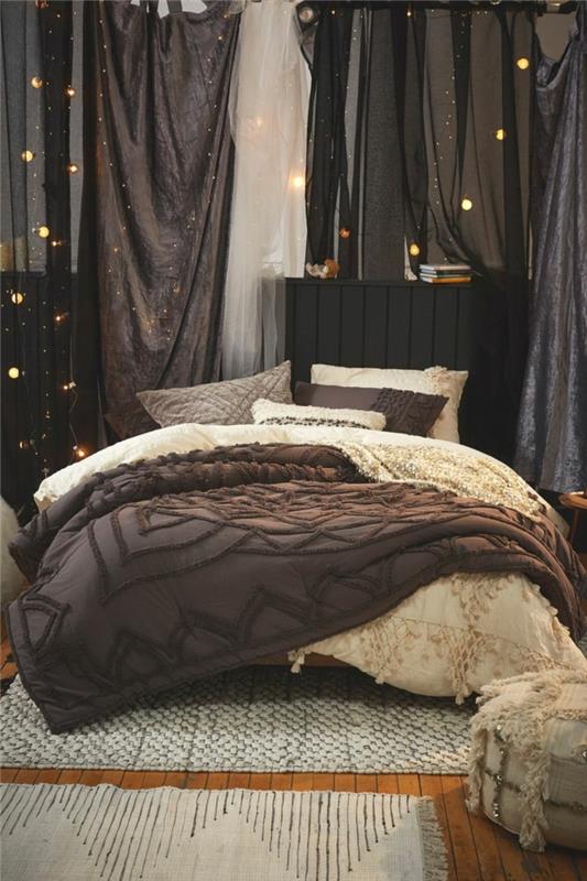 plokšti austi kilimai, didelė lova, papuošta rudais ir kreminiais patalynės užvalkalais, styginiai žibintai, pilka anglis