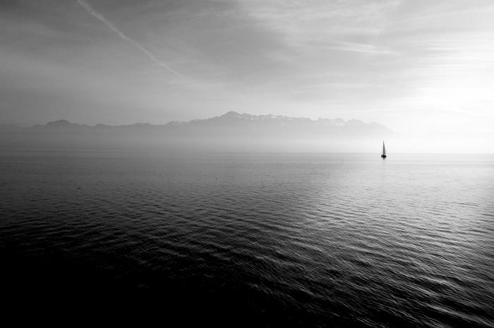 oddaljena silhueta jadrnice, ki plava v mirnih morskih vodah, črno -bela fotografija morske pokrajine