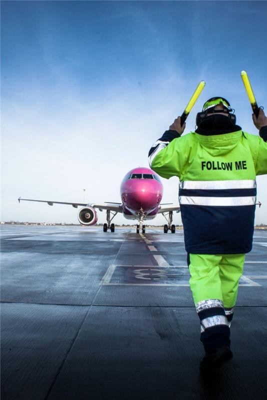 moški, ki dela na letališču v svojih vidnih delovnih oblačilih, reflektorska jakna s pisavo