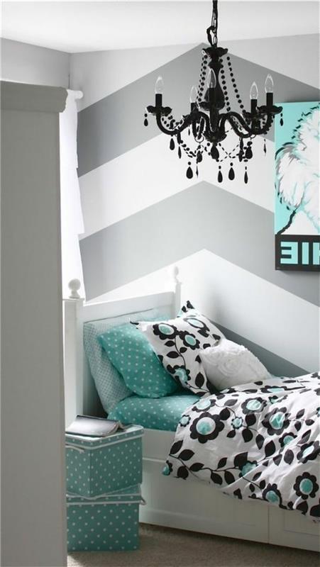 gėlių motyvai juodai ir žaliai, ant baltos lovos su žalsvai mėlyna patalyne ir pagalve, dryžuotos sienos baltos ir pilkos spalvos miegamajame, puošni juoda baroko stiliaus liustra