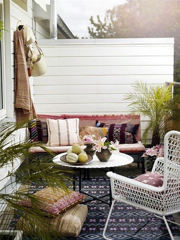 dört renkli minderli kanepe, beyaz yuvarlak masanın yanında ve beyaz sandalye, ön veranda dekoru, desenli kilim ve saksı bitkileri