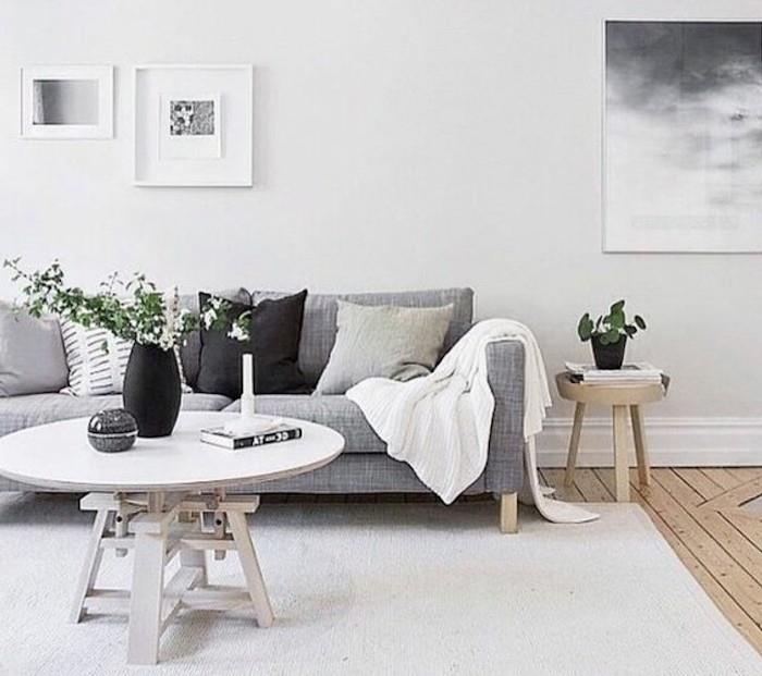 baltas kilimas, kabantis įrėmintas menas, pilka sofa, pilka ir juoda, pagalvės, medinis žurnalinis staliukas, jaukios svetainės