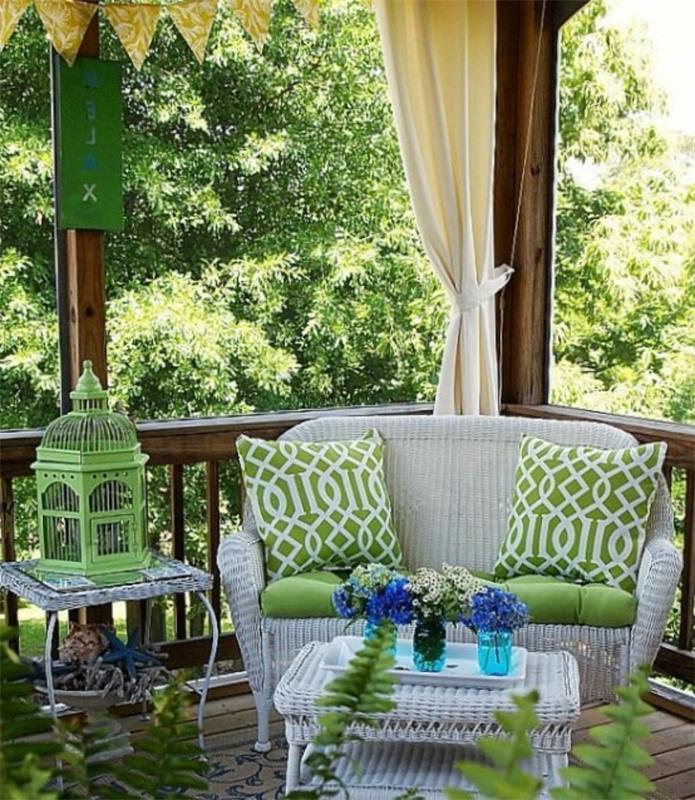 Soluk gri hasır kanepe, biri dekoratif yeşil metal kuş kafesi, diğeri tepside çiçekli ağaç vazolar, kapalı veranda fikirleri, ahşap kirişler ve perdeler, yeşillikler ve saksı bitkileri ile iki uyumlu masa ile