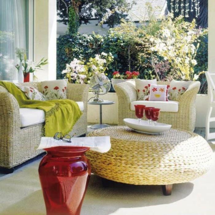 hasır mobilyalar, kanepe ve rahat sandalye ve yuvarlak masa, yastıklar ve battaniye, büyük kırmızı vazo ve süslemeler ile ön sundurma dekoru içeren bir sette