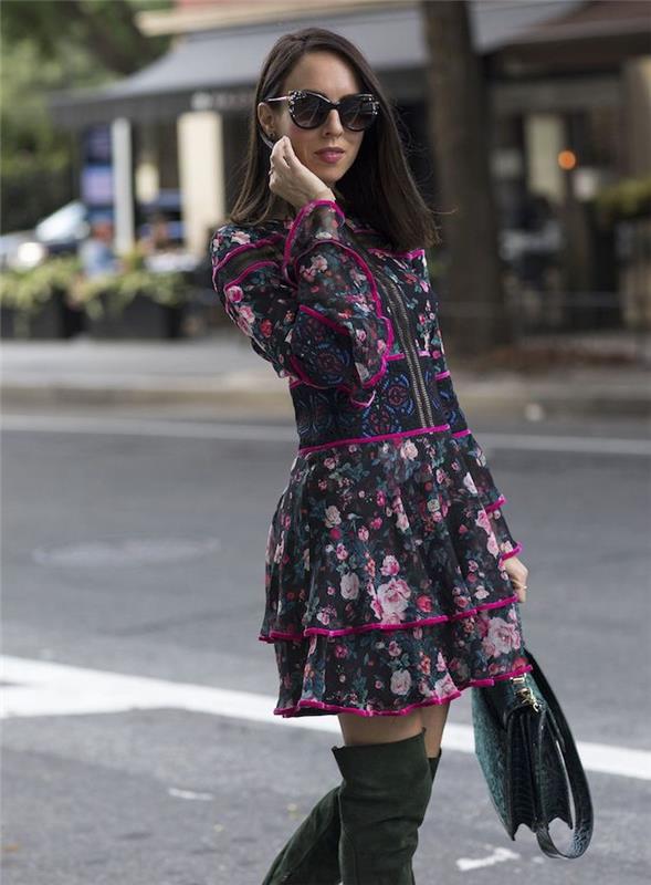 ženska, ki hodi po ulici, oblečena v obleko s cvetličnimi motivi, škornje do kolen in sončna očala, modni trendi