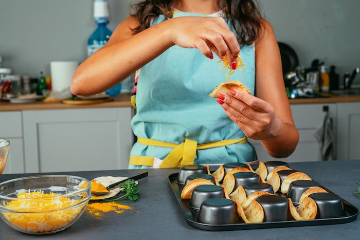 taco mėsos receptas, moteris su raudonu nagų laku, sūrio uždėjimas, ant tortilijų įvyniojimų, mėlyna prijuostė, juodas stalas