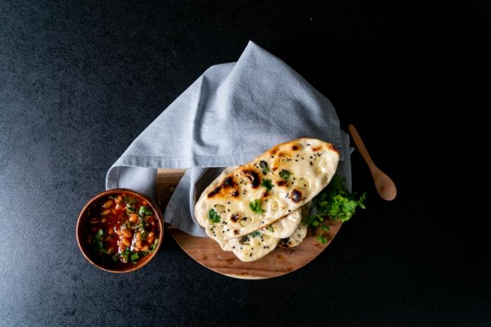 naan ekmeği, tahta kesme tahtasına yerleştirilmiş, üstüne mavi bez, ahşap kasede domates soslu fasulye