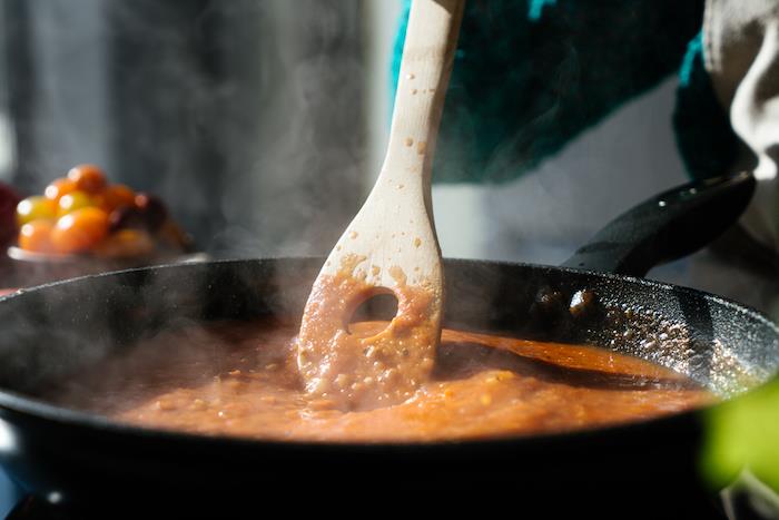 pomidorų tyrė juodojo padažo keptuvėje, sumaišyta su medine mentele, pomidorų sriubos receptas, neryškus fonas