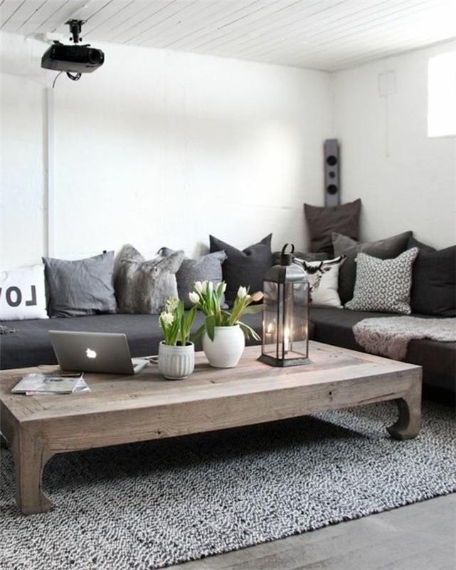 didelis medinis stalas, pilka kampinė sofa, daugybė pagalvių, pilkas kilimas, populiarios svetainės spalvos